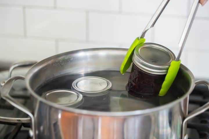 Submerging jars of homemade jam in boiling water to process.