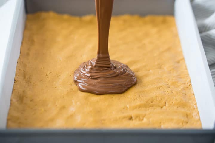 Pouring melted chocolate over peanut butter bars.