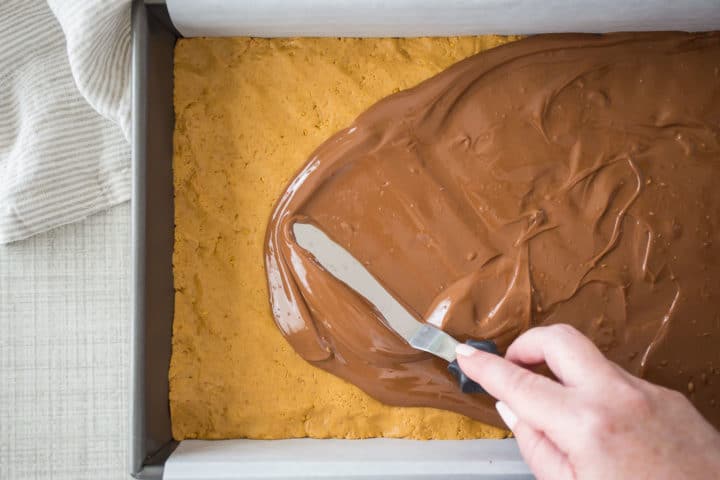 Spreading melted chocolate over peanut butter bars with a small offset spatula.