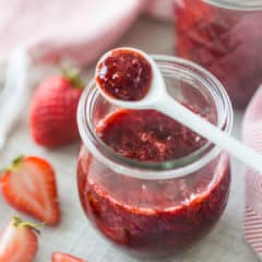 Small jar of homemade strawberry jam with a white ceramic spoon.