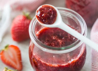 Small jar of homemade strawberry jam with a white ceramic spoon.