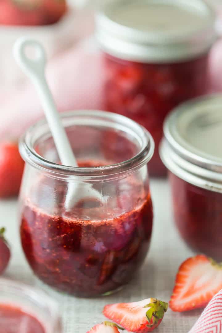 Jars of homemade strawberry jam, surrounded by fresh strawberries.