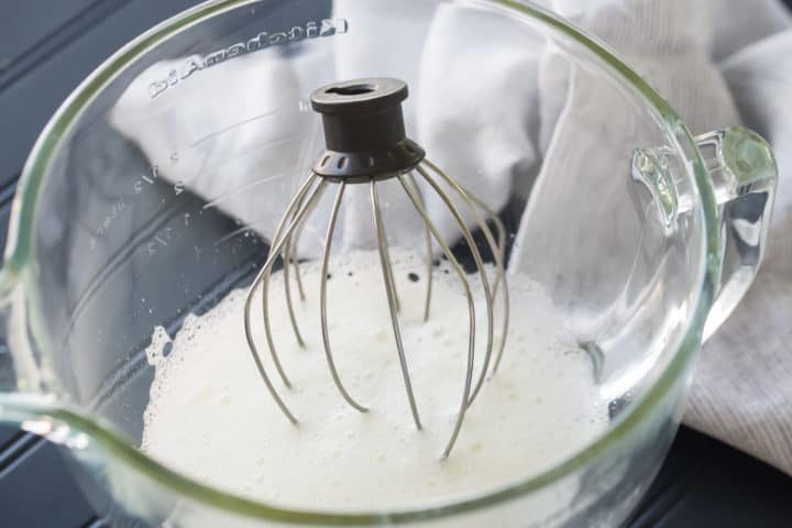 Foamy egg whites in a glass bowl with a whisk.