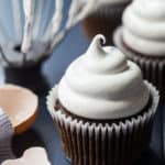 Marshmallow frosting on a cupcake with a whisk in the background.