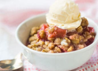 Small bowl of rhubarb crisp with a scoop of vanilla ice cream, on a pink printed napkin.