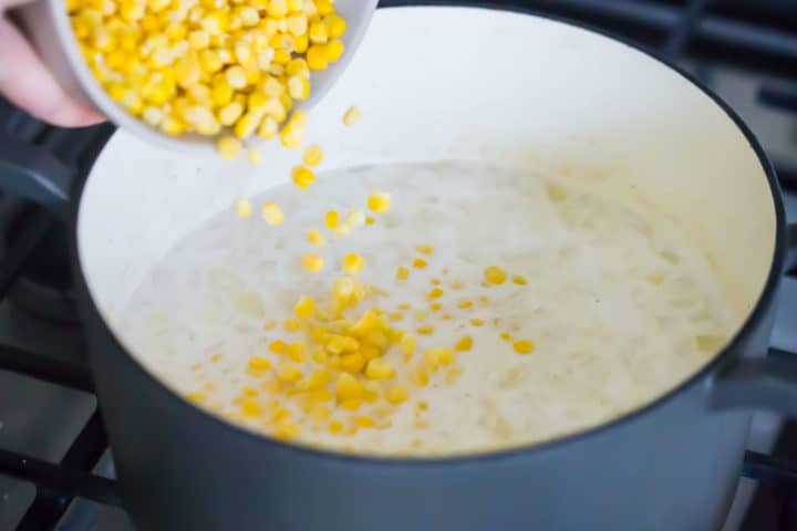 Adding corn to a pot of homemade corn chowder.