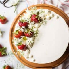 Overhead image of a strawberry shortcake cake with strawberries and fresh flowers, on a wooden cake stand.