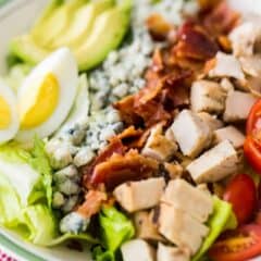 Close-up image of a large bowl of cobb salad, with all the components arranged in neat rows over a bed of greens.