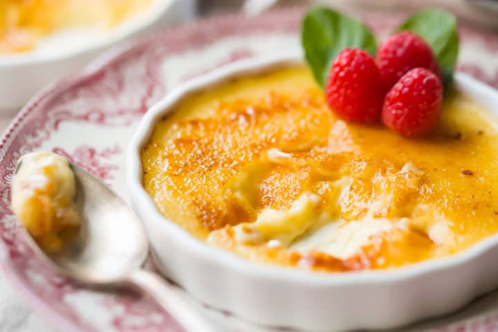 Close up image of a partially eaten creme brulee, with a crackly sugar top and smooth custard below.