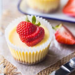 Mini cheesecakes made in a cupcake pan, with graham cracker crust and a fresh strawberry garnish.