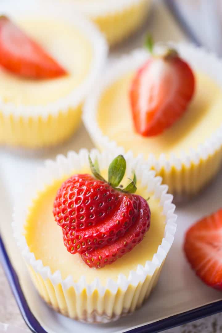 Mini cheesecakes on a blue-rimmed tray, with sliced strawberries on top.