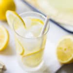 Tall glass of lemonade with ice and slices of fresh lemon.
