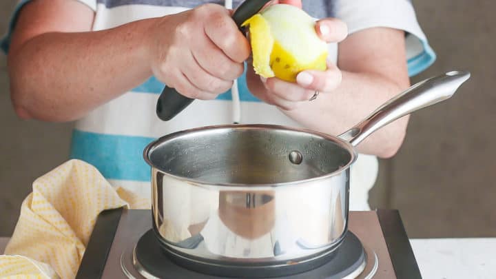 Removing zest from a lemon with a vegetable peeler.