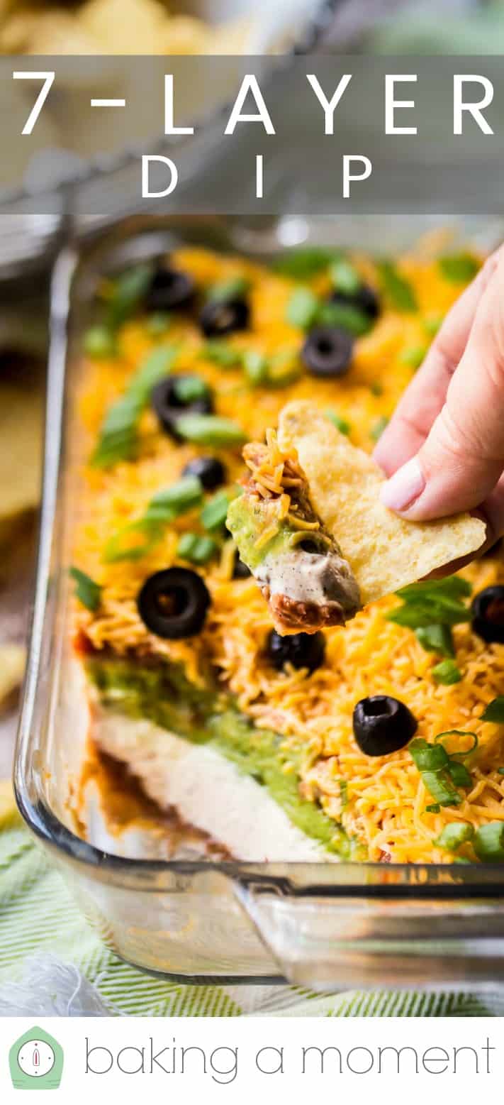 Close-up image of a tortilla chip taking a scoop out of a dish of 7-layer Mexican dip, with a text overlay above that reads "7-Layer Dip."