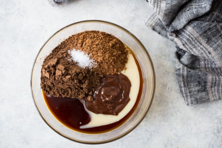 Condensed milk, melted chocolate, cocoa, vanilla, and salt in a glass bowl.