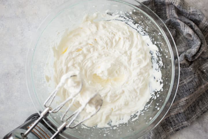 Large bowl of whipped cream with an electric hand mixer.