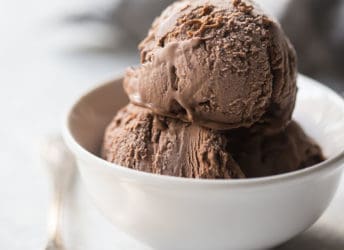 Chocolate ice cream in a small white bowl with a silver spoon, on a white background.