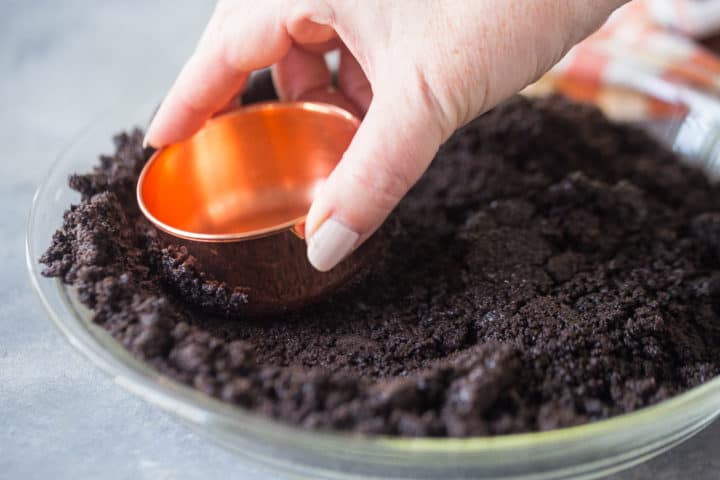 Pressing Oreo cookie crust into a pie pan with a copper measuring cup.