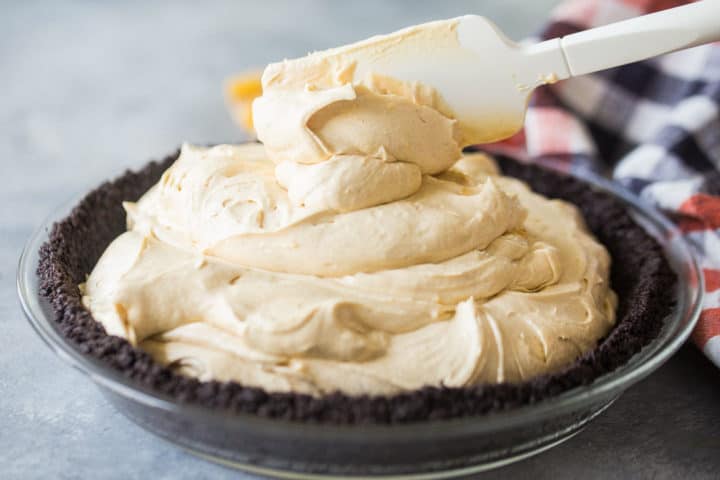 Spooning peanut butter mousse filling into an Oreo cookie crust.