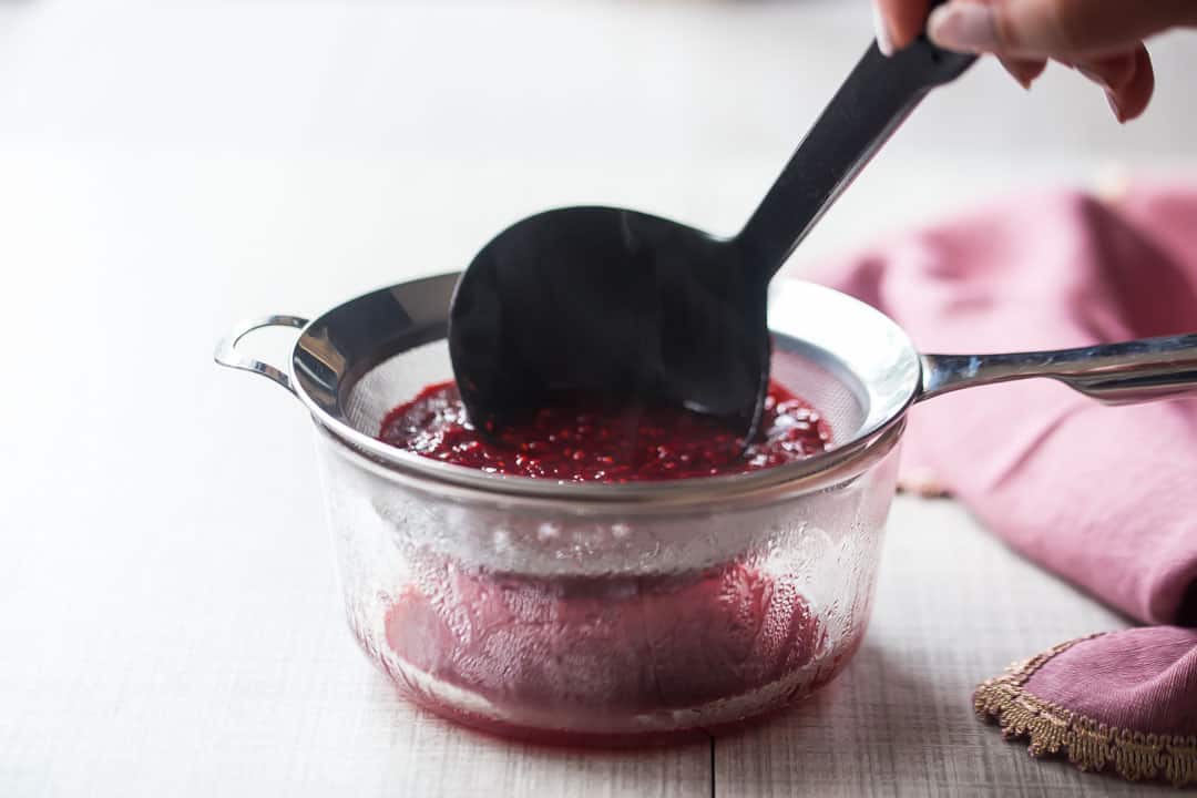 Pushing raspberry sauce through a sieve with a ladle, to remove the seeds.