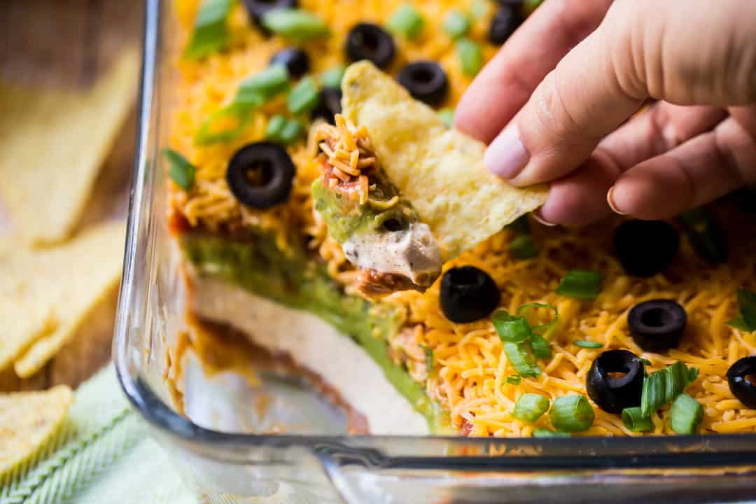 Scooping 7-layer taco dip with a corn chip.