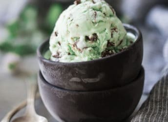 Homemade mint chocolate chip ice cream in a dark brown bowl, on a gray background.
