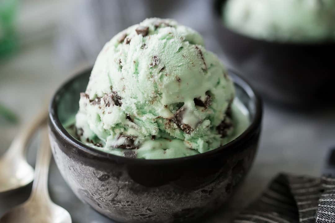 Dark brown bowl with mint chocolate chip ice cream recipe and vintage silver spoons.