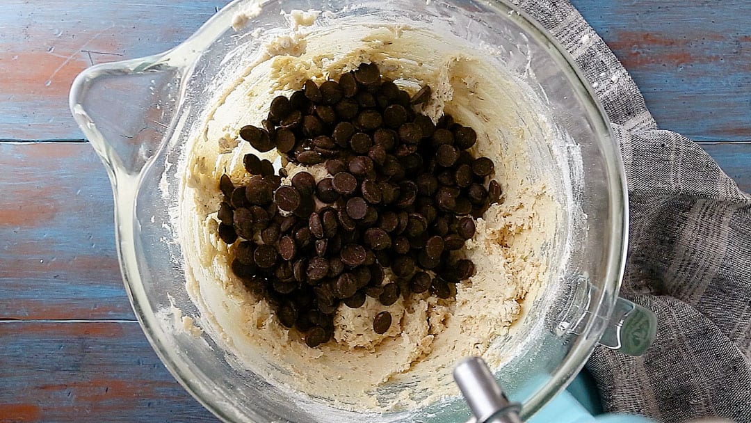 Chocolate chips and oatmeal cookie dough in a large glass mixing bowl.