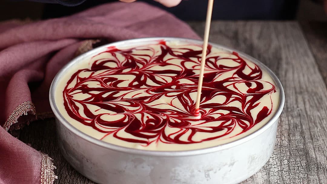 Swirling raspberry sauce into cheesecake batter with a wooden skewer.