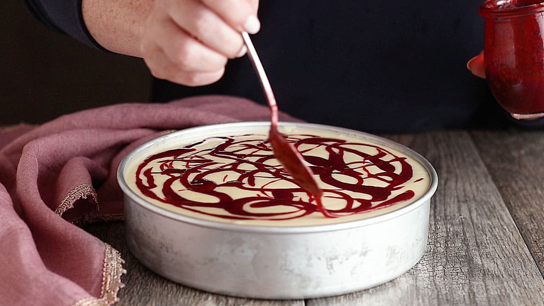Drizzling raspberry sauce over cheesecake.