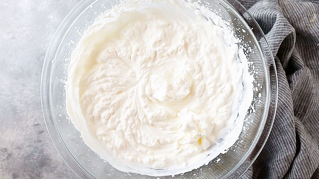 Overhead image of a bowl of stiffly whipped cream, on a gray background.