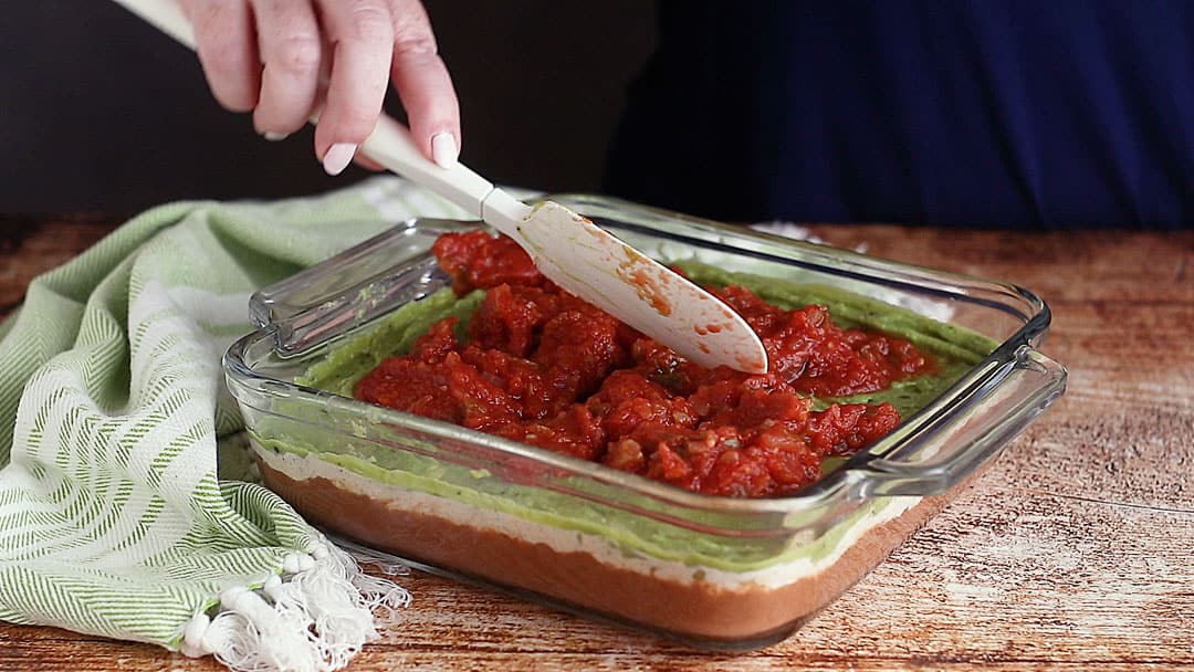 Layering salsa over guacamole for 7-layer dip.