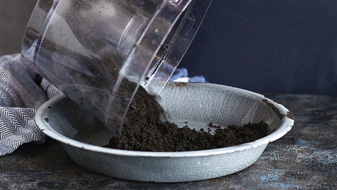 Pouring oreo crust mixture into a pie dish.