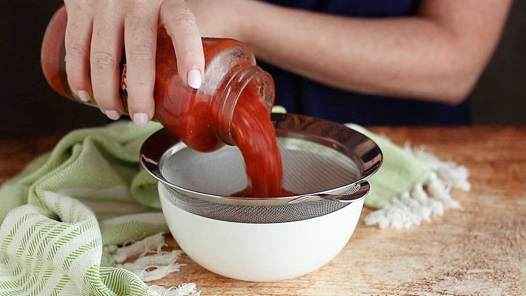 Pouring salsa through a fine mesh strainer.