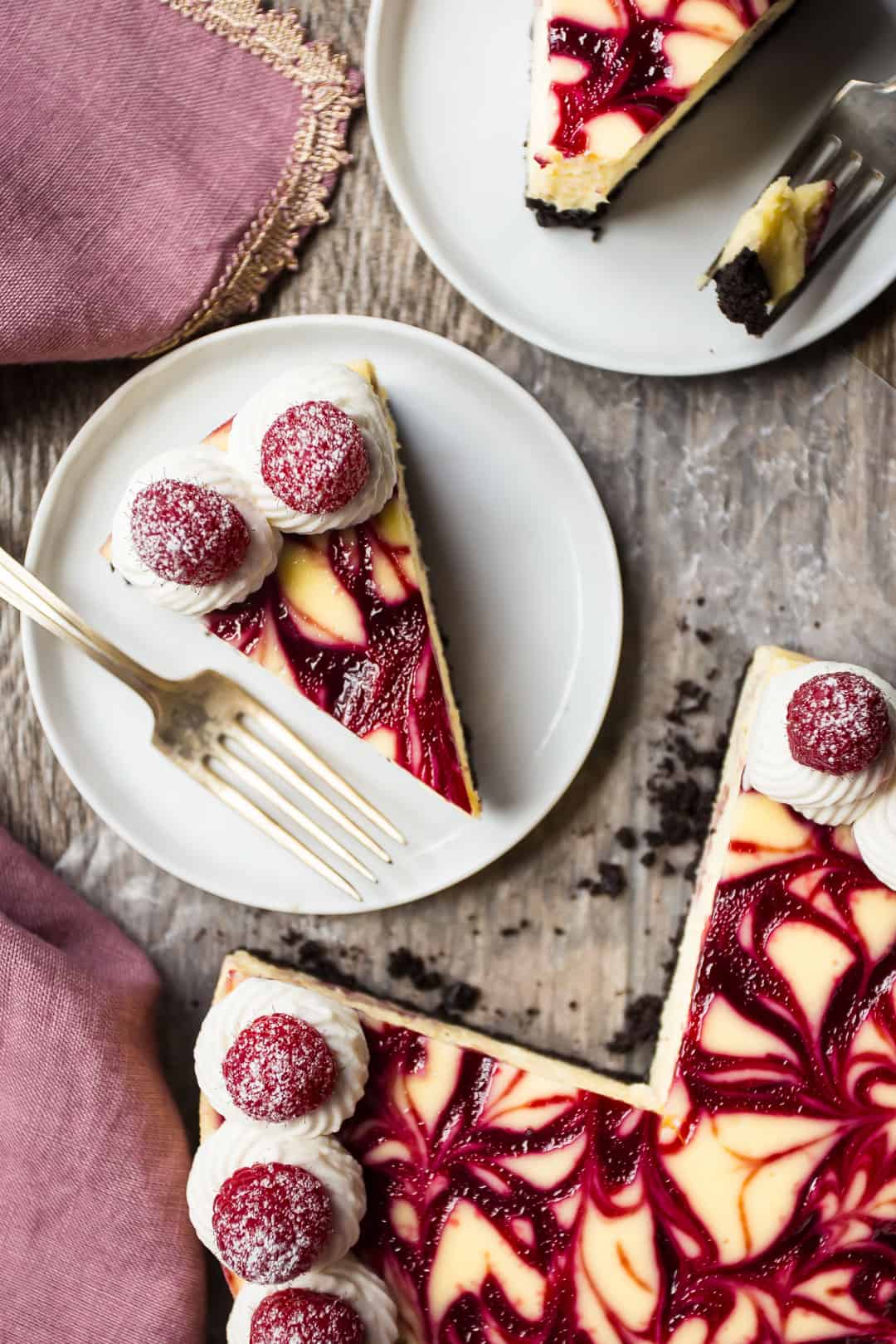 Overhead image of white chocolate raspberry cheesecake with slices on white plates with silver forks.
