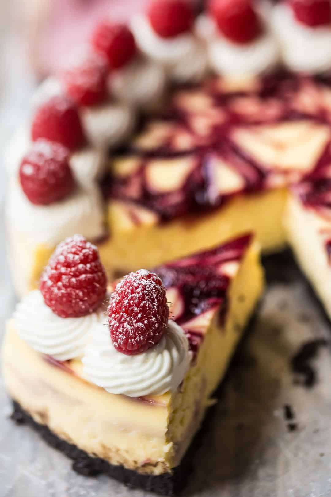 White chocolate raspberry cheesecake slice on a distressed wood table.