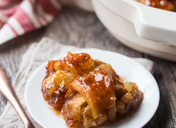 Two apple dumplings on a white plate with a copper fork and a linen napkin in the background.