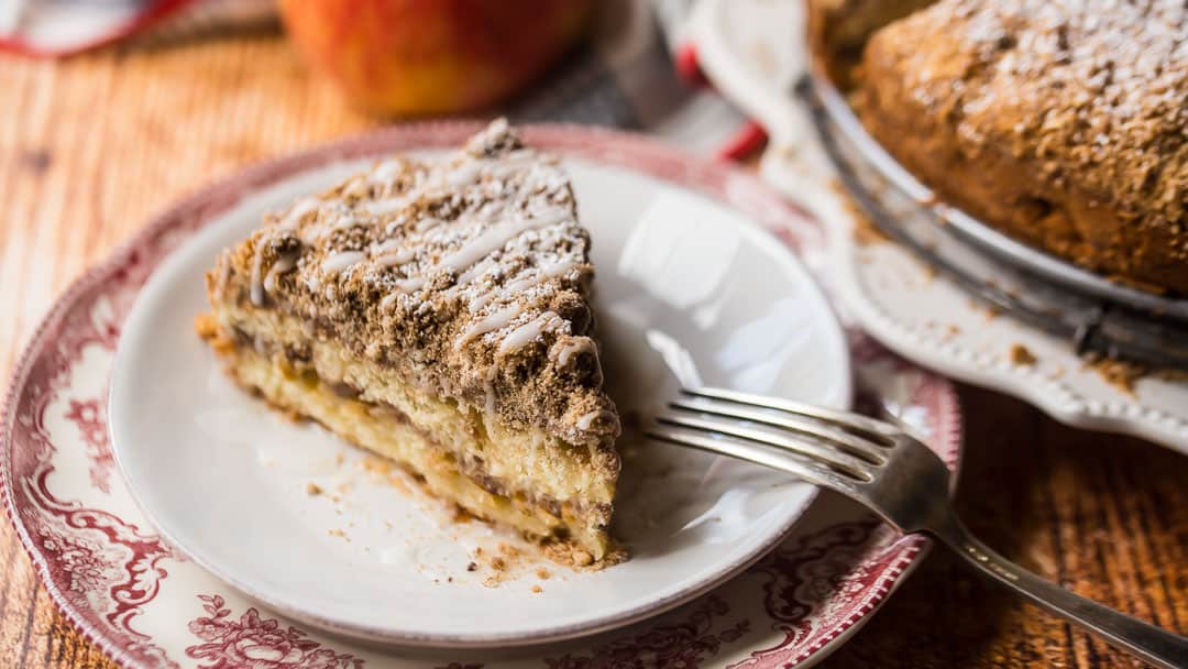 Slice of sour cream apple coffee cake on a dessert plate with a vintage silver fork.