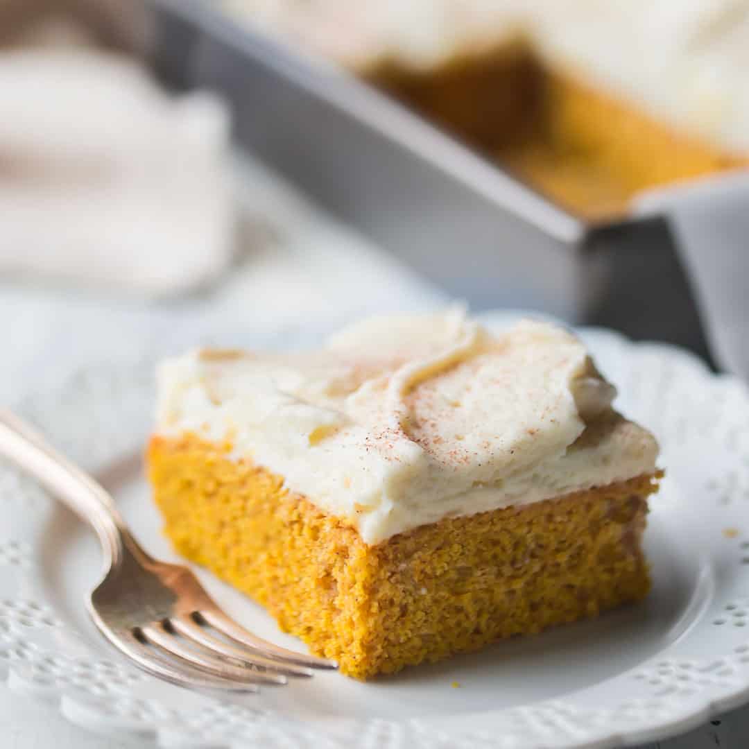 Square slice of pumpkin cake with cream cheese frosting and cinnamon on top, on a white background.