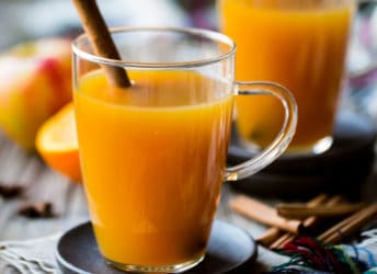 Two glass mugs of hot apple cider with cinnamon sticks.