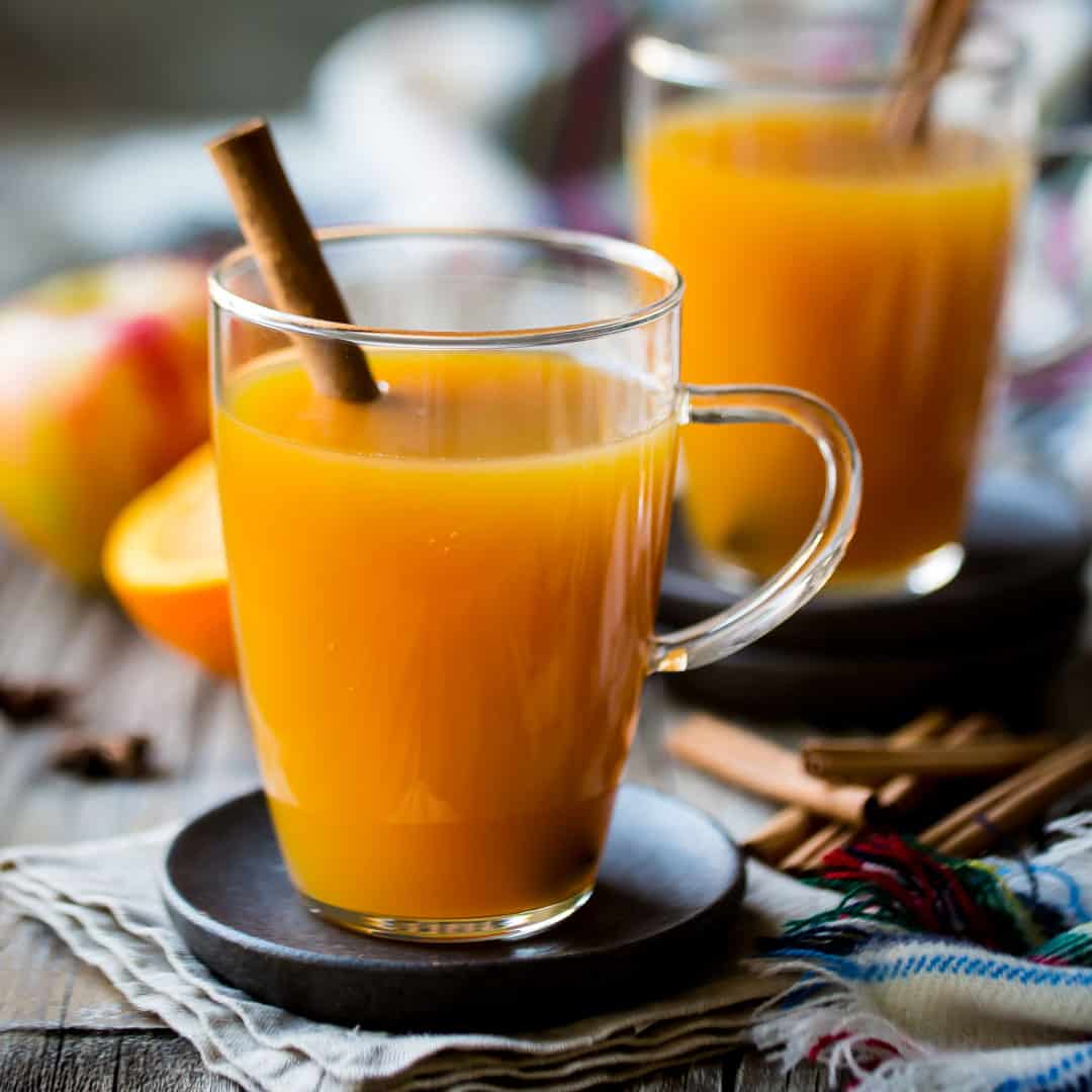 Two glass mugs of hot apple cider with cinnamon sticks.