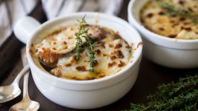 French onion soup in white crocks with melted cheese and fresh herbs.