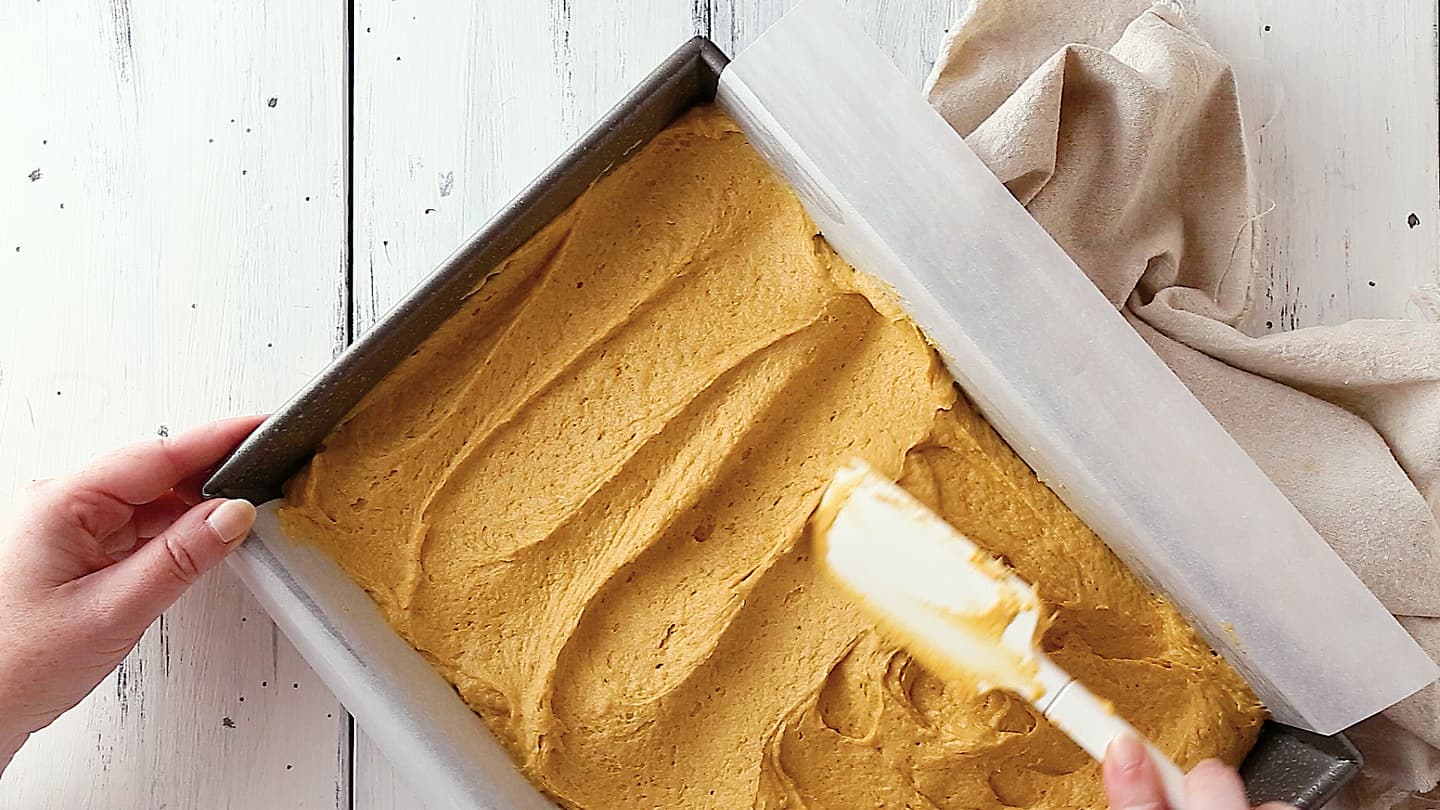 Smoothing pumpkin cake batter in a 9x13-inch pan with a silicone spatula.