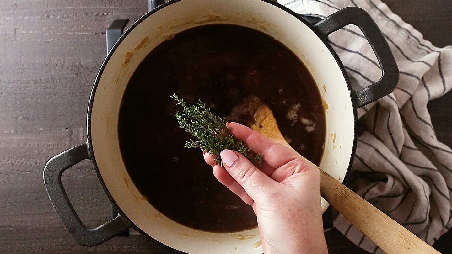 Adding fresh thyme to a pot of French onion soup.