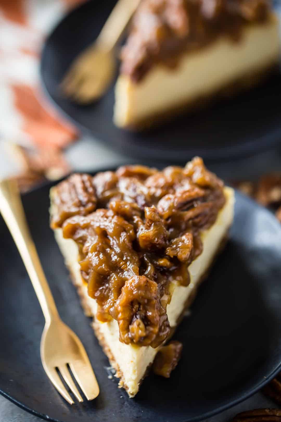 Pecan pie cheesecake recipe (can also be baked as pecan pie cheesecake bars) on a dark plate with a gold dessert fork.