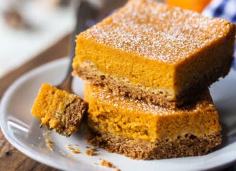 Pumpkin gooey butter cake bars stacked on a white plate on a wood board.