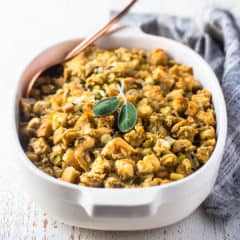 Thanksgiving stuffing recipe baked in a white casserole dish with fresh sage and a gray cloth in the background.