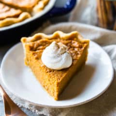 A slice of sweet potato pie on a white plate, with whipped cream and cinnamon.