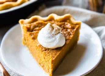 A slice of sweet potato pie on a white plate, with whipped cream and cinnamon.