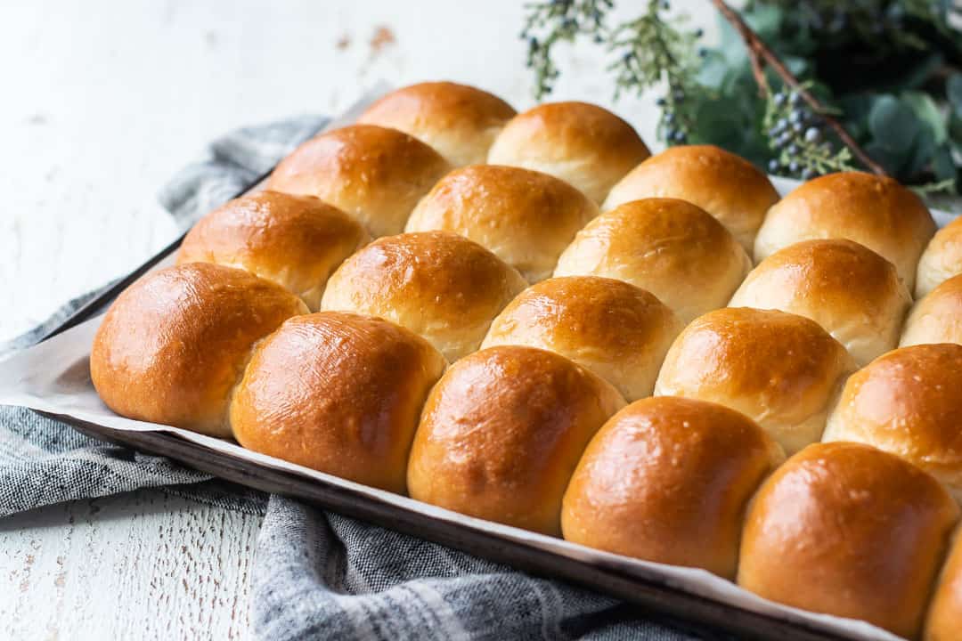 Tray of freshly baked easy dinner rolls, on a gray cloth with greenery in the background.